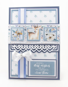 A Christmas card with a star backing paper, a deer image, presents and Christmas Roses